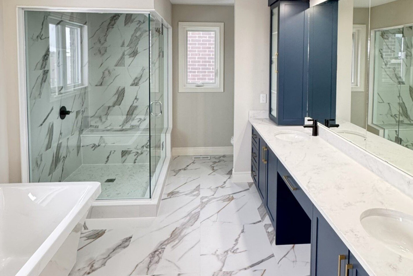 Ensuite with quartz double vanity, freestanding tub and a marble-tiled glass shower
