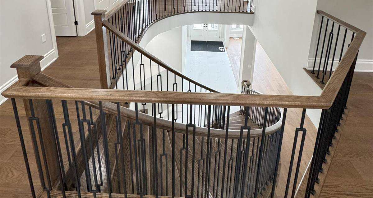 Curved staircase with iron spindles and hardwood flooring on the second floor of a Scarlett Homes home