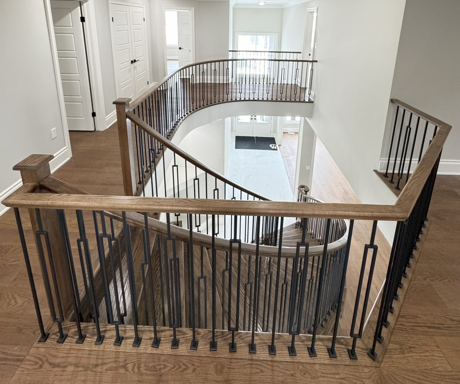 Second-floor landing with hardwood flooring overlooking a curved staircase finished with iron spindles