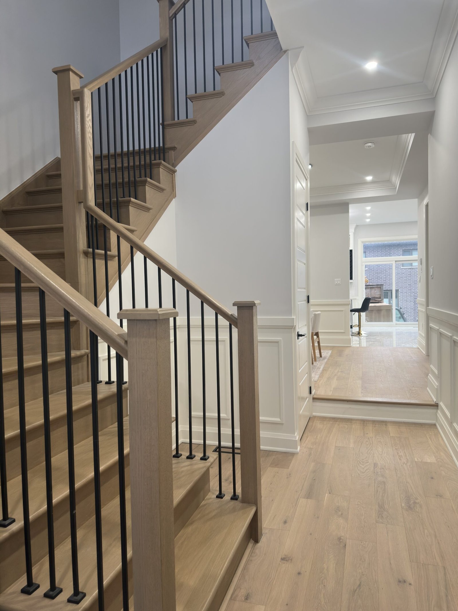 Stained oak staircase with black iron spindles rising from a hardwood hallway in a Scarlett Homes single-detached home