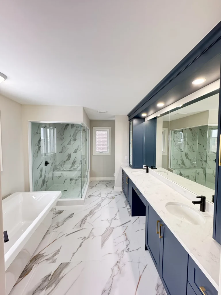 Primary ensuite with a long navy vanity, freestanding tub and glass shower