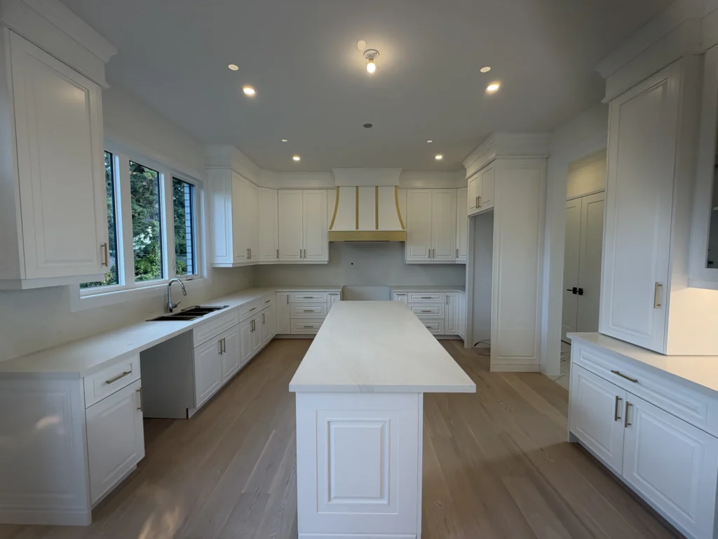 White kitchen with a centre island, range hood with brass trim and engineered hardwood floors