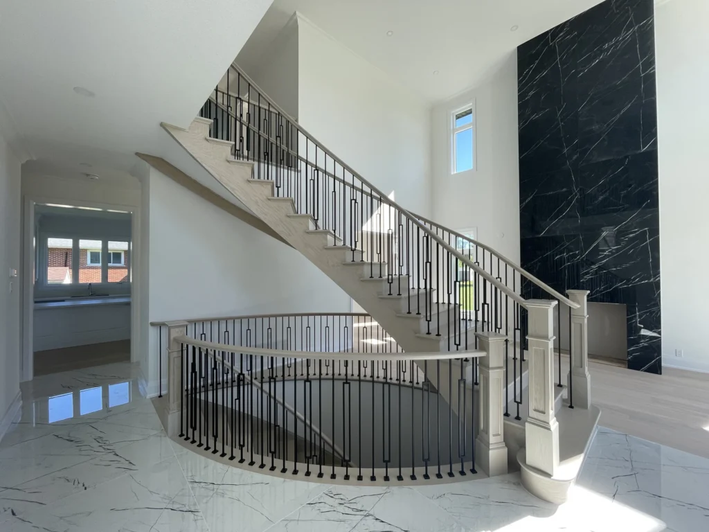 Curved staircase beside a black marble feature wall in an open-to-above foyer