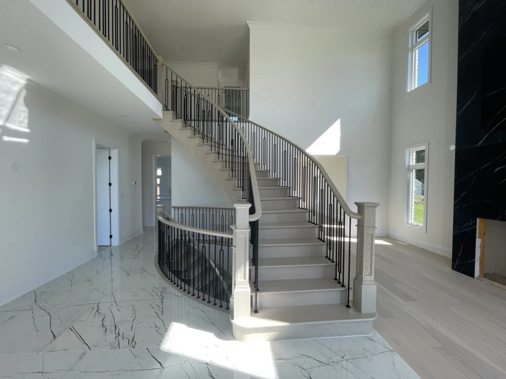 Front view of a curved staircase with iron spindles and porcelain tile foyer