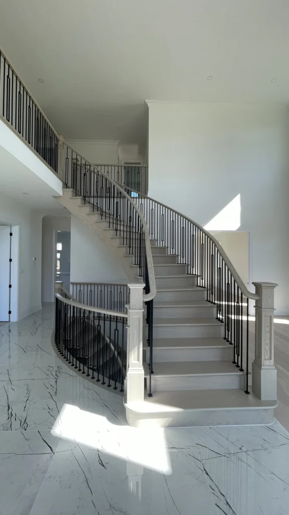 Full-height curved staircase with iron spindles in a bright foyer